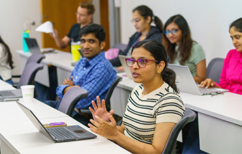 Classroom with people engaged in discussion, one woman speaking.
