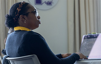 Person working on a laptop, wearing a dark sweater and a leopard-print headband.