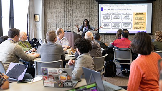 A woman presents to a group in a conference room setting with a screen displaying a presentation slide.