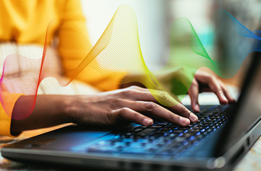 Person typing on a laptop keyboard beneath colorful translucent wave-like graphics